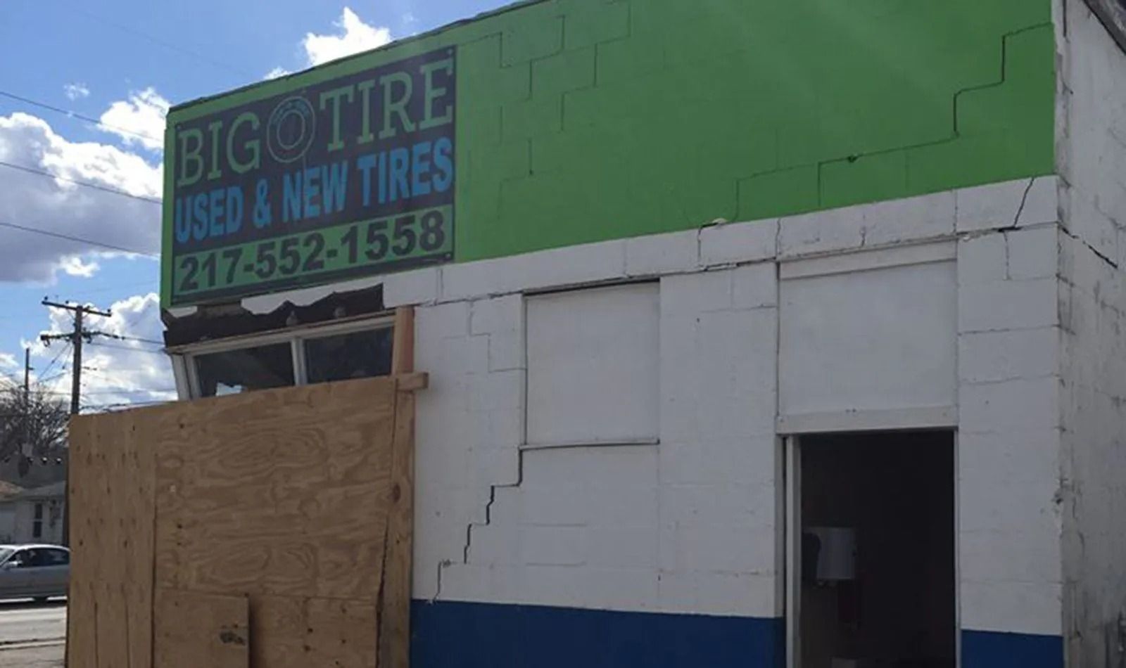 Big O Tire building with boarded-up windows and damage; green and white exterior with blue trim.
