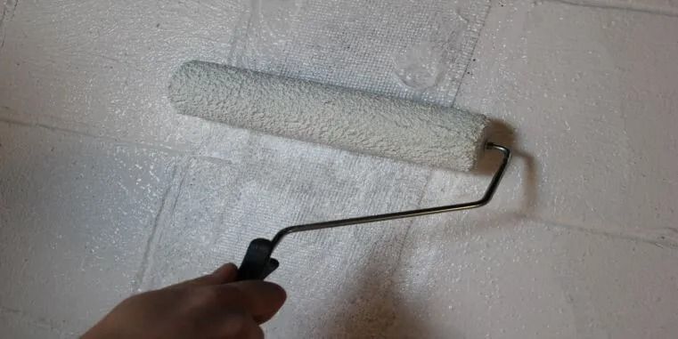 A person is painting a wall with a paint roller, applying a coat of white paint.