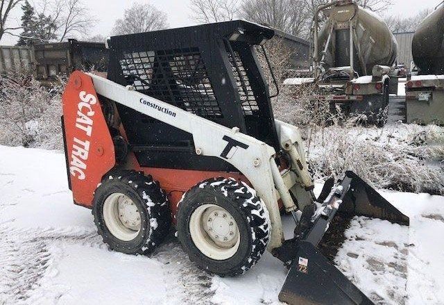 Scat Trak skid steer loader with snow on the ground; orange and white machine with a black cab.