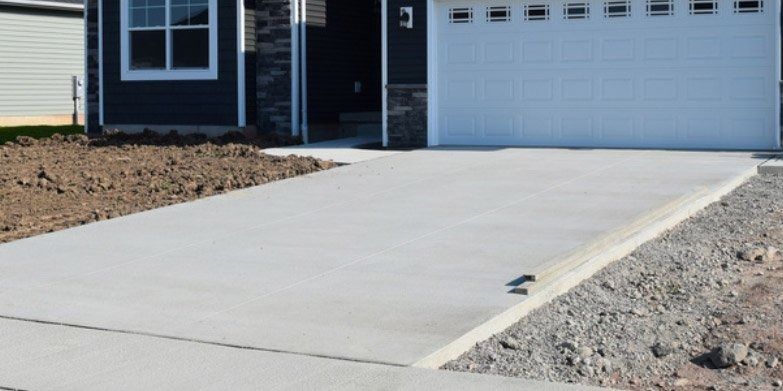 A gray concrete driveway in front of a house with a white garage door.