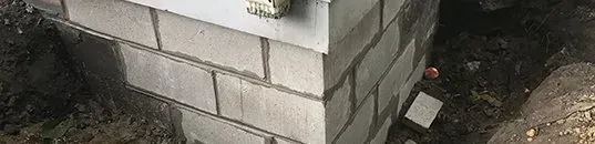 Corner of a light-colored brick wall with mortar, on a dark, earthy surface with an object.