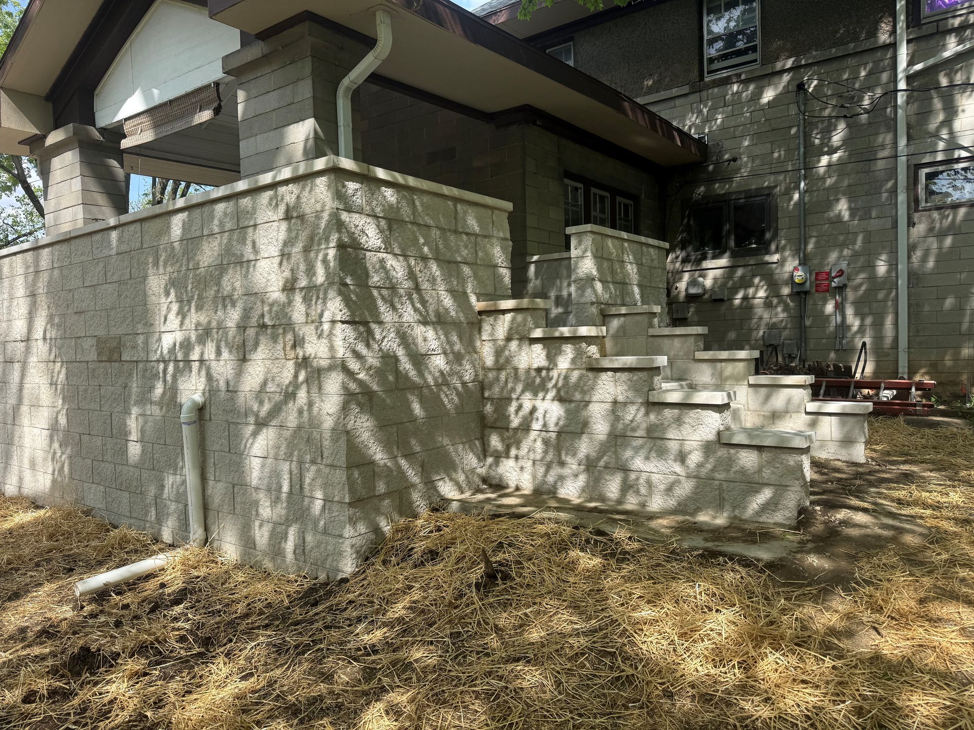 Stone house exterior with front steps, white wall, and dry leaves in the yard