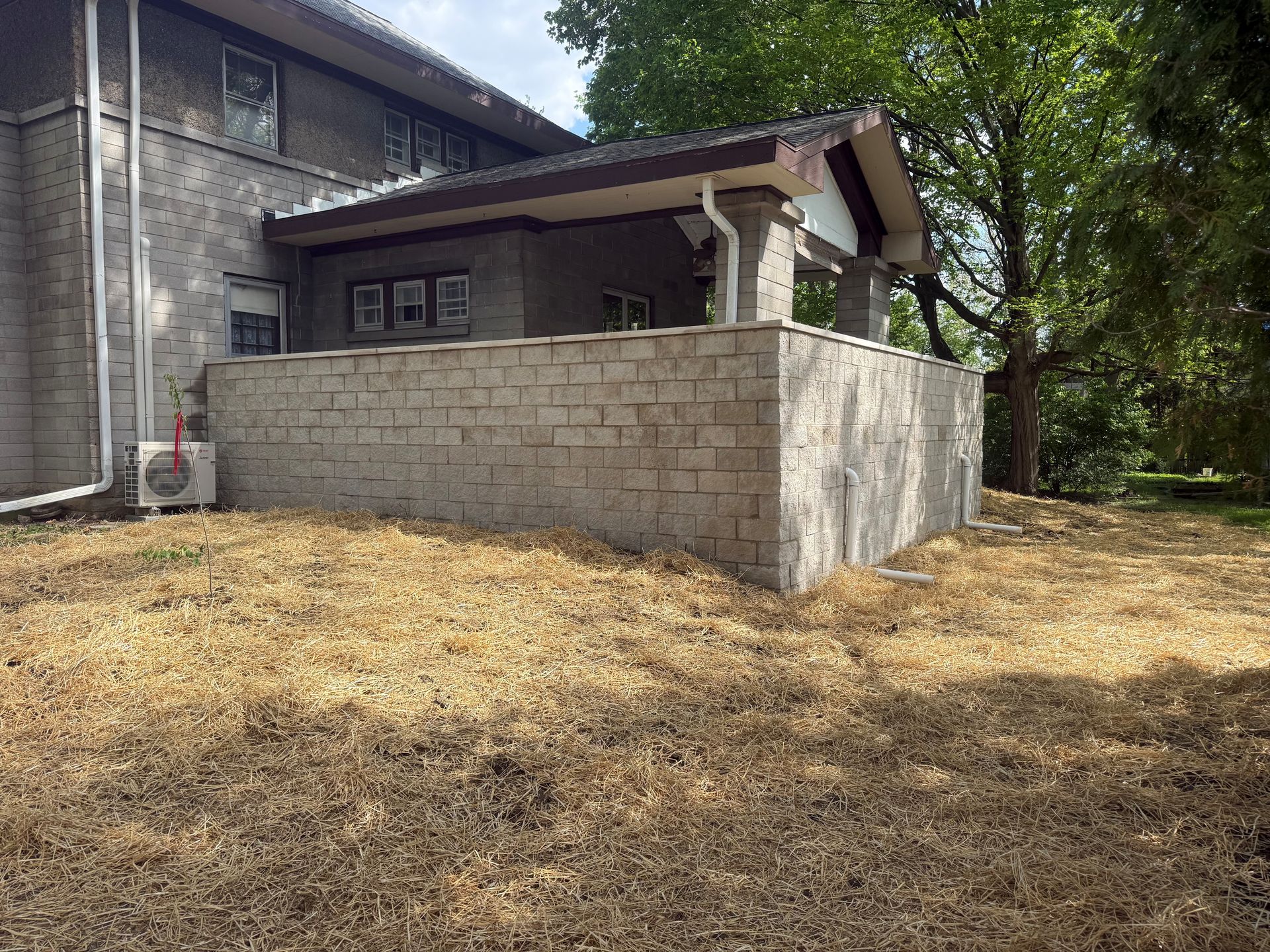Small stone-walled patio beside a house, with a covered porch and dry yard trees behind.