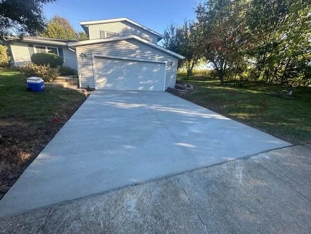 Newly poured concrete driveway leading to a garage. House in background, blue sky, and green lawn.