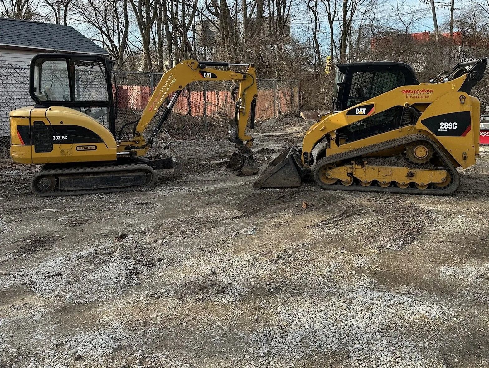 Yellow excavator and skid steer on a gravel lot near a building.