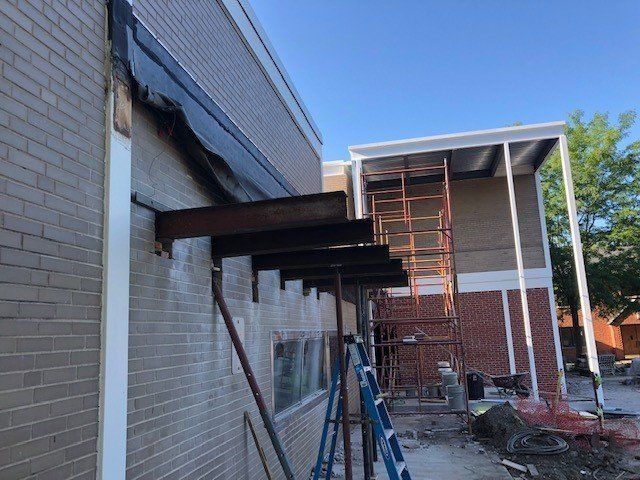 Building construction: Steel beams extending from a brick wall with scaffolding. Blue ladder in foreground.