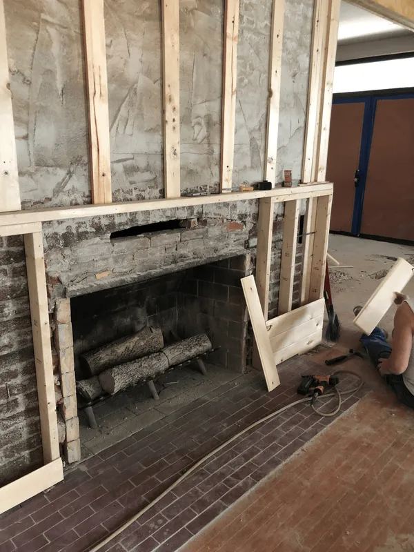 Fireplace under renovation with exposed brick, framing, and logs inside.
