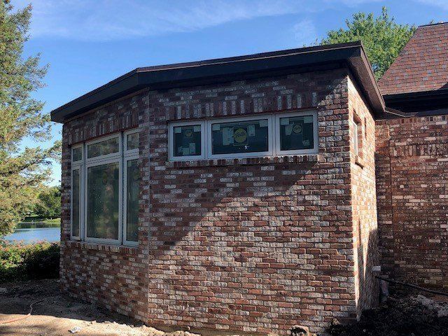 Brick exterior of a house with windows and a dark brown roof under a blue sky.