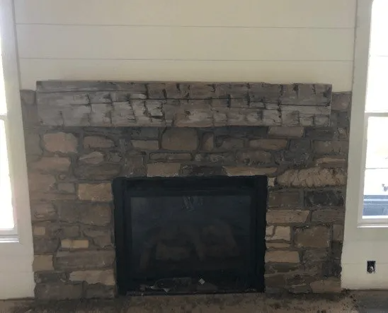 Stone fireplace with black interior and white planked wall above.