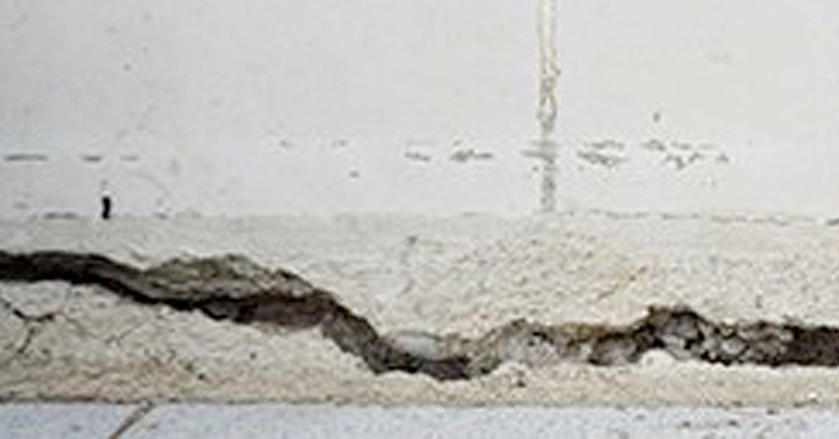 Close-up of a damaged wall with a large, deep crack revealing the interior, with crumbling plaster.