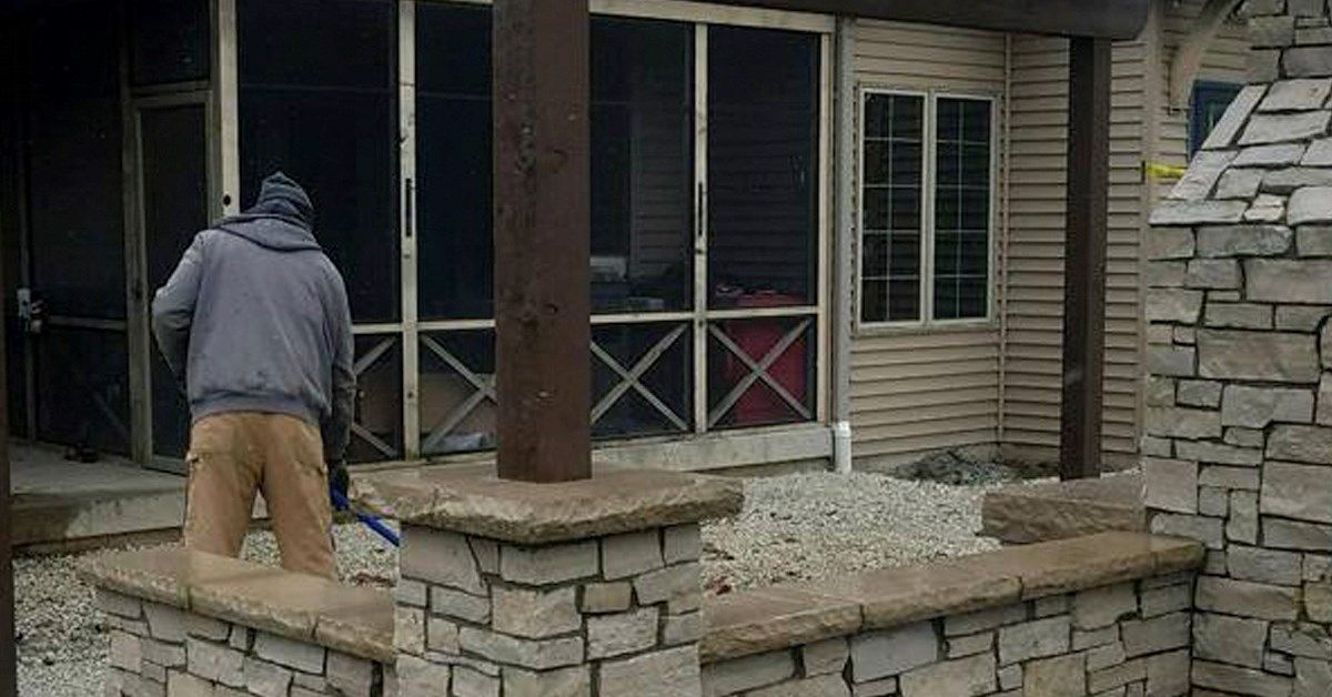 Person sweeping patio near stone wall and screened porch.