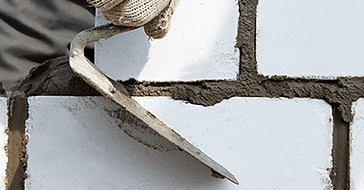 Hand with trowel applying mortar between white bricks.