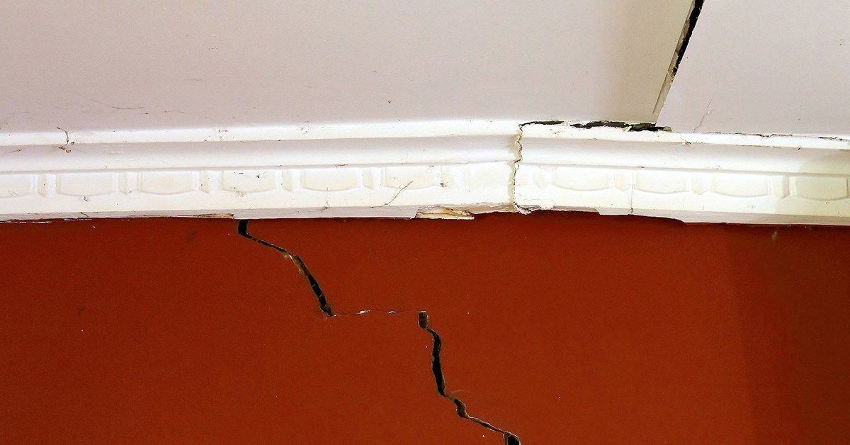 Cracked orange wall with white molding and a damaged ceiling.