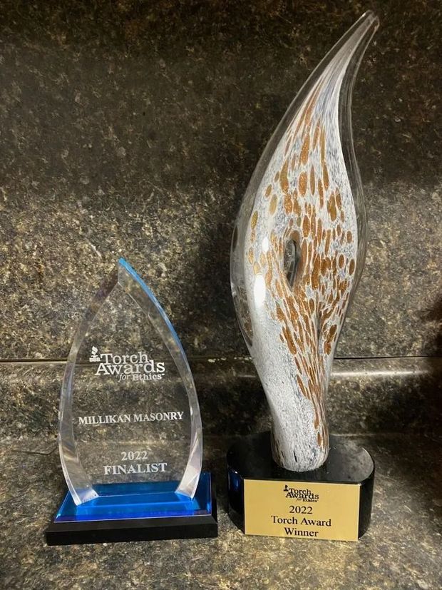Two awards on a counter. One is a clear acrylic flame shape, the other is a glass art piece with brown and white swirls.