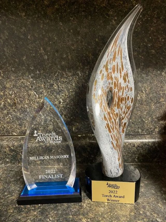Two awards on a counter. One is a clear acrylic flame shape, the other is a glass art piece with brown and white swirls.