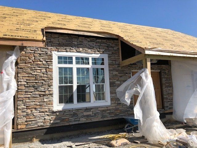 Exterior of house under construction with stone veneer siding, and a white window.