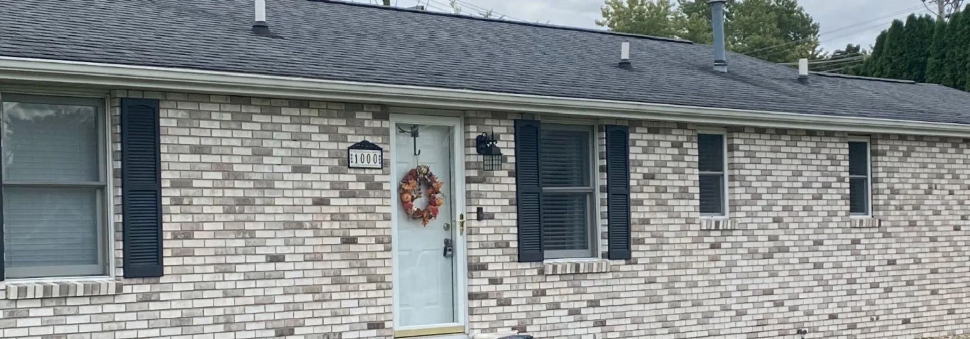 Brick house with gray roof, black shutters, and a front door with a wreath.