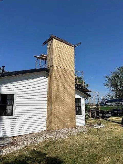 Brick chimney extending from a white house; scaffolding surrounds. Blue sky overhead.