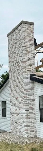 Brick chimney on a white house with a dark gray roof. The chimney has a dark cap.