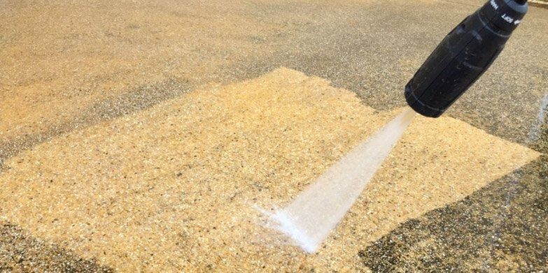 A pressure washer cleaning a light-colored aggregate surface.