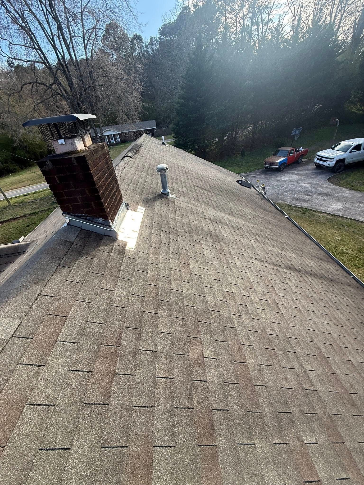 Rooftop with chimney, shingled surface, and parked cars below in a wooded area