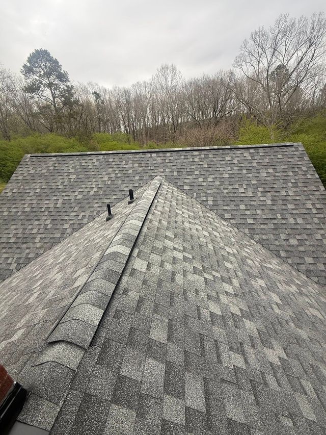 Gray shingled roof with a front gable, viewed from above with trees in the background