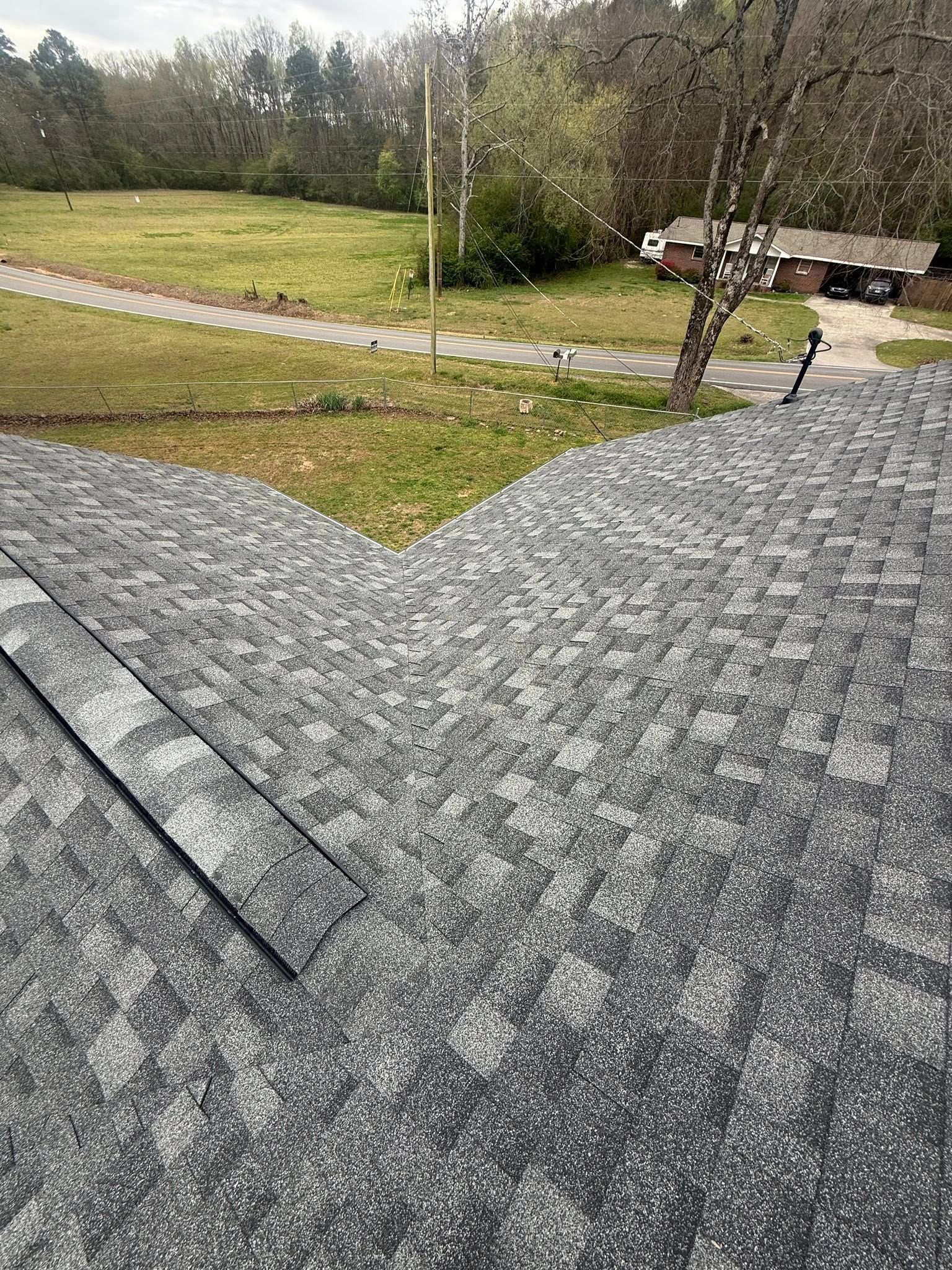 Roof shingles overlooking a grassy yard, winding path, trees, and a bench in the distance.