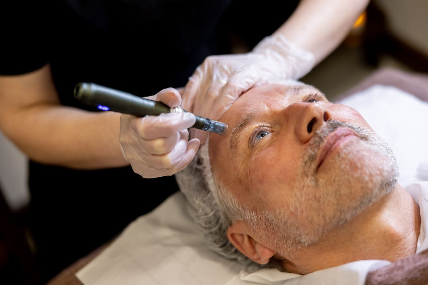 Cosmetic treatment being applied to a man’s forehead with a handheld device while he reclines