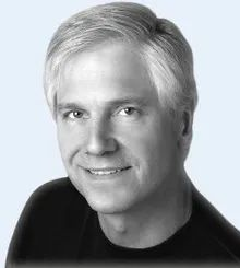 Black-and-white portrait of a smiling man with light hair, wearing a dark shirt, against a light background