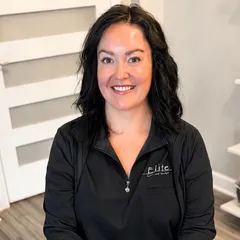 Smiling woman in black top standing indoors with hands clasped
