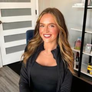 Woman smiling in a black outfit seated in a modern office with a door and shelving behind her
