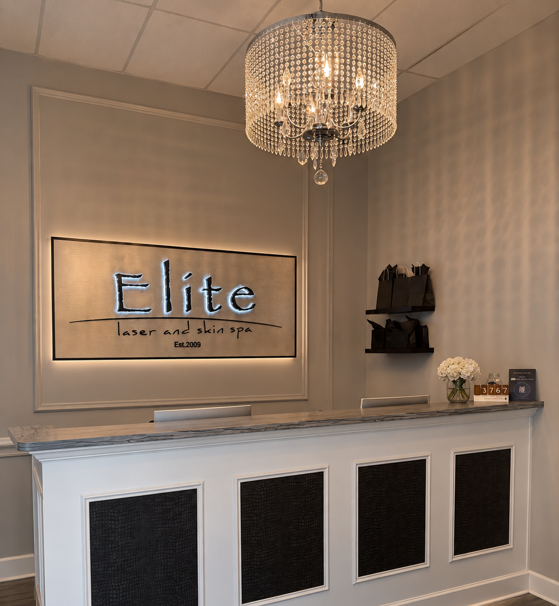 Modern hotel reception desk with chandelier, illuminated “elite” sign, and dark wall panels