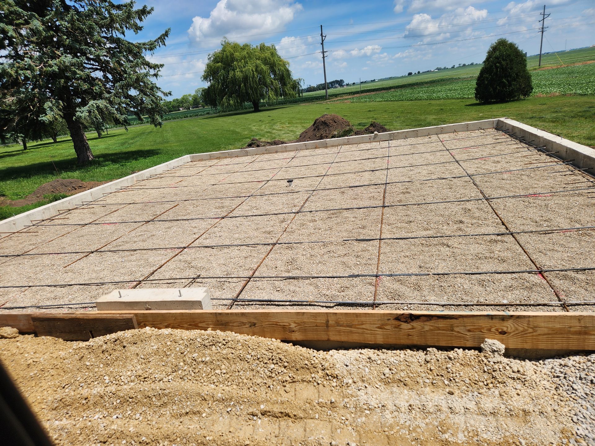 A concrete foundation is being built in a field with trees in the background.