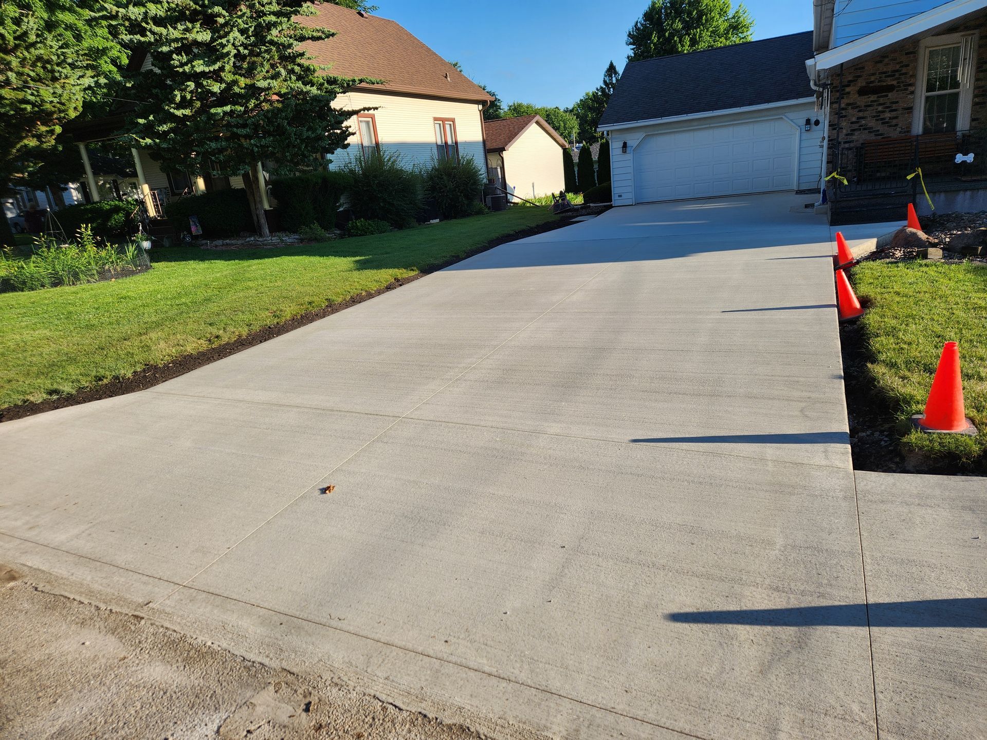 Driveway at a suburban house with orange cones marking the right edge near the lawn.