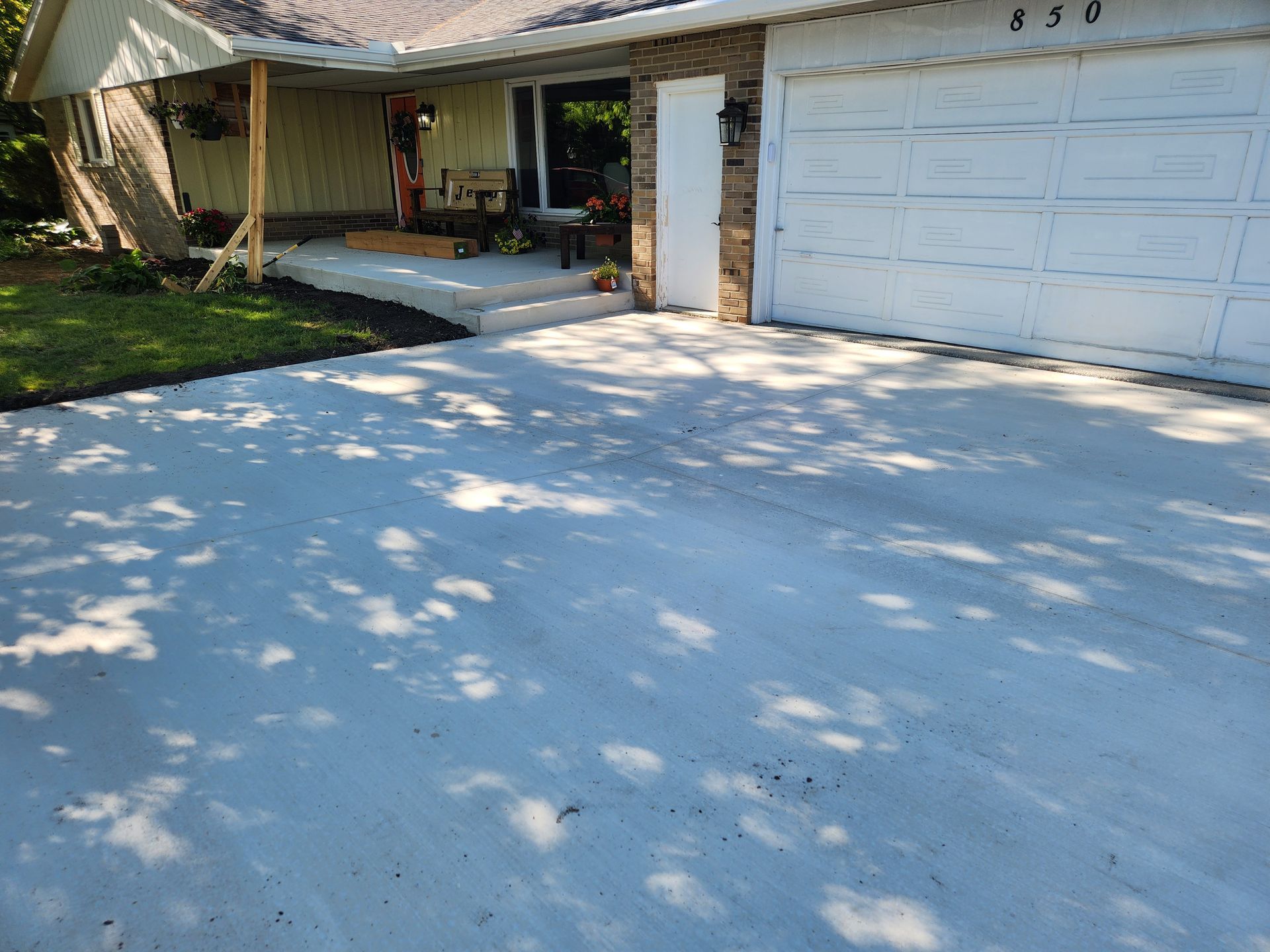 Freshly poured white concrete driveway leading to a suburban house with a garage and front porch.