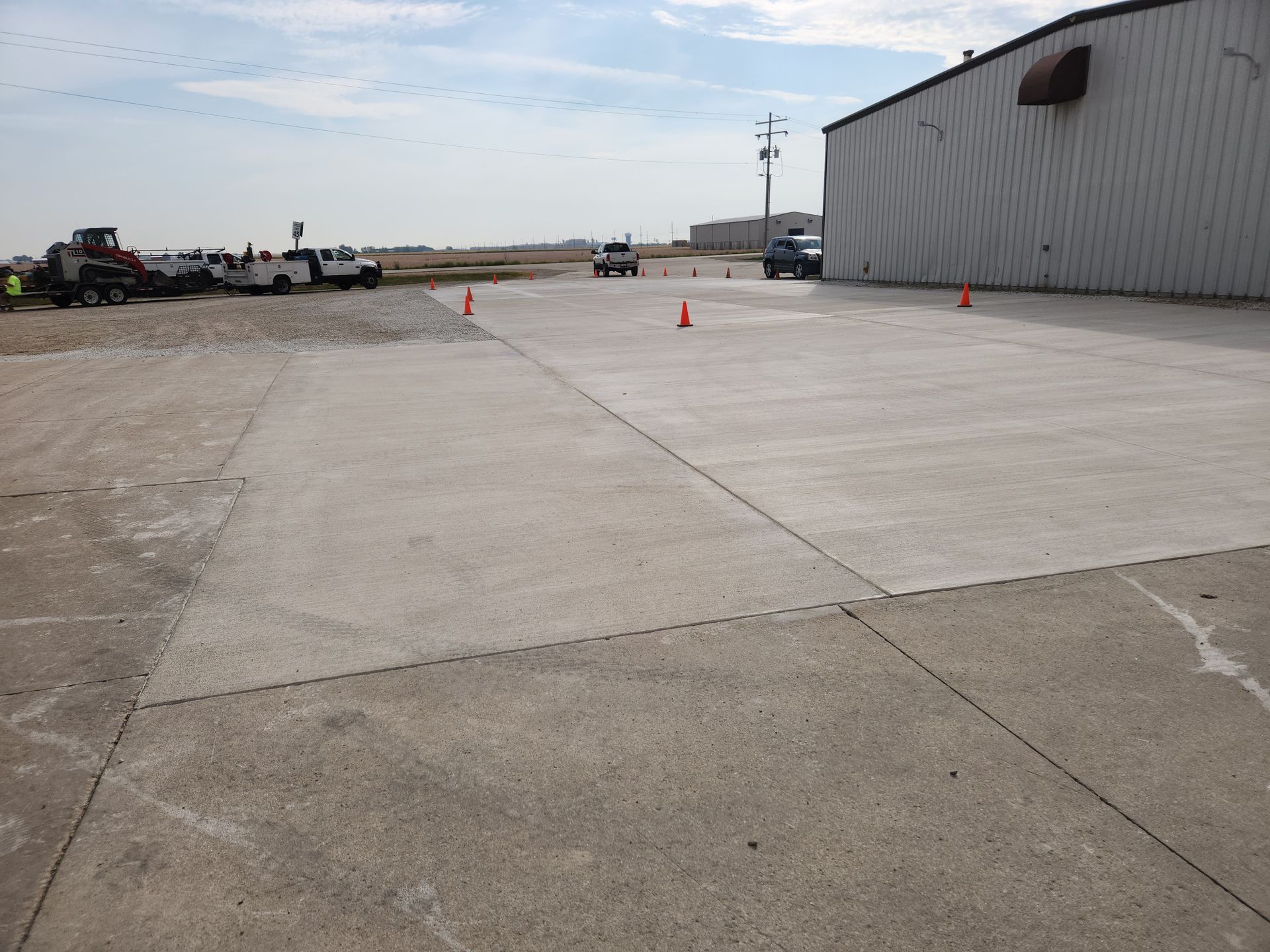 Concrete surface with vehicles and cones near a building. Outdoor setting, overcast sky.