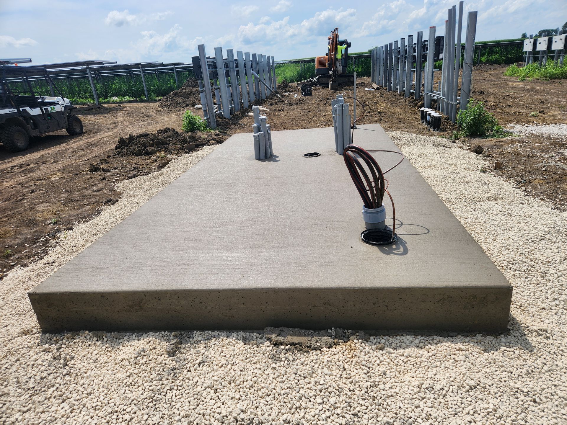 Concrete pad with metal poles and cables, likely for solar panel installation, in a field.
