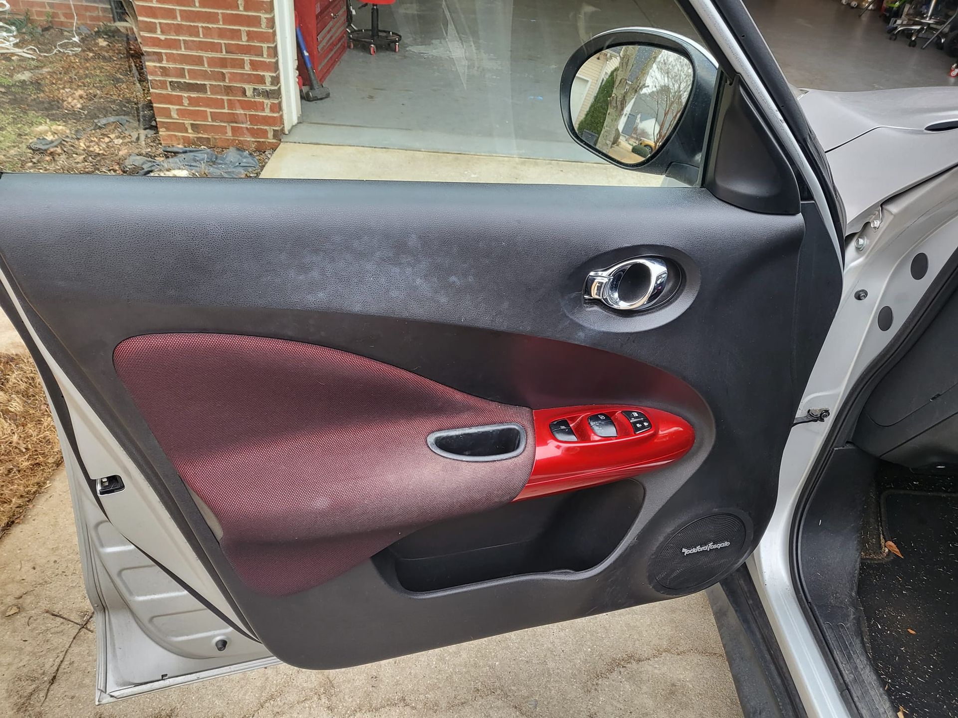 A silver car with the door open is parked in front of a garage.