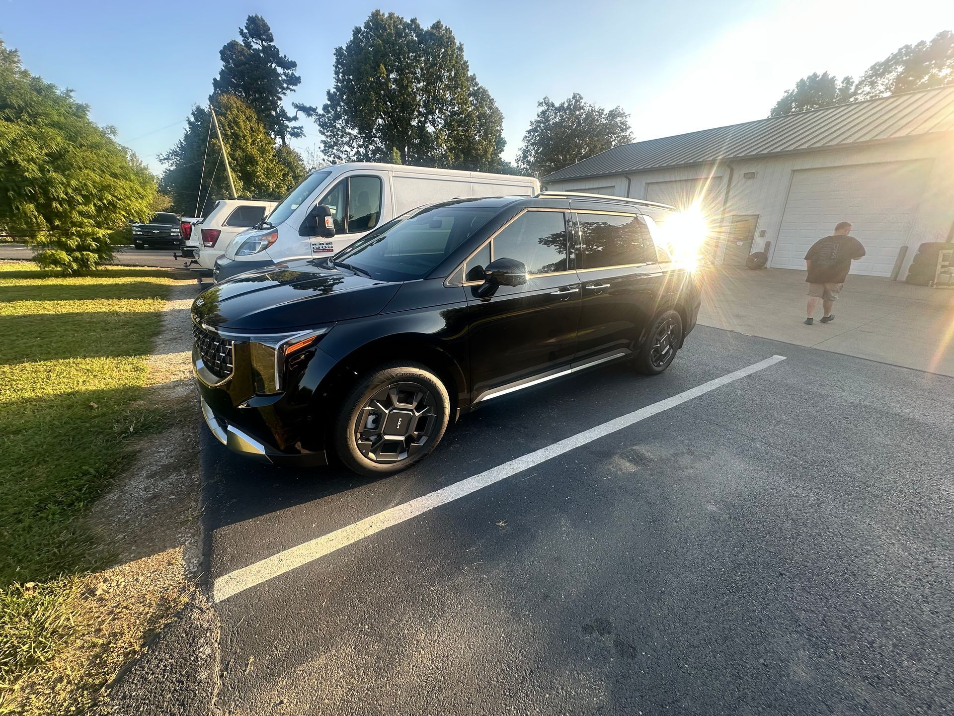 Black SUV parked in a lot, sunlight in background, person walking near garage.