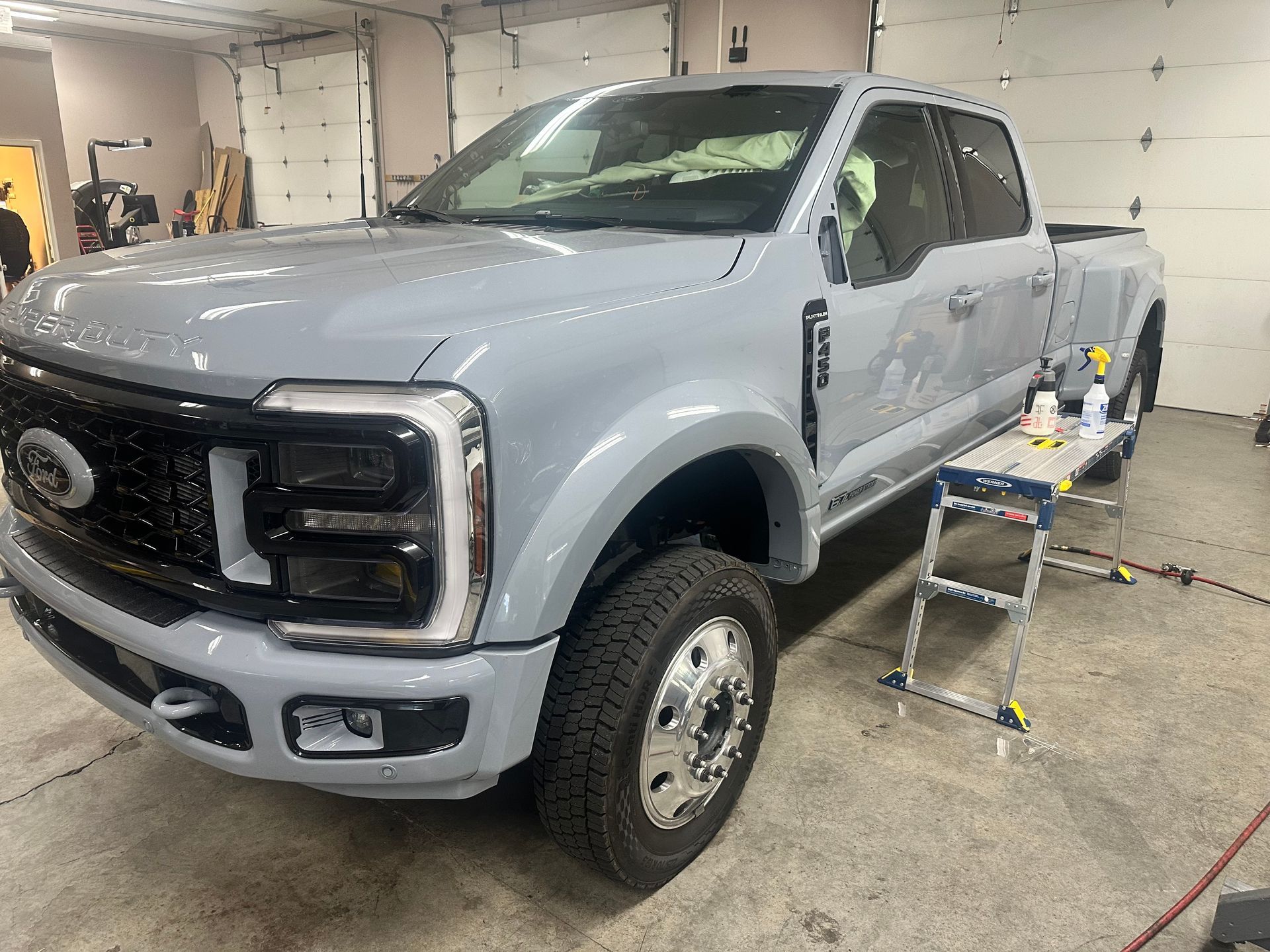 Gray Ford Super Duty truck in a shop, with black grill, silver wheels, and work table.