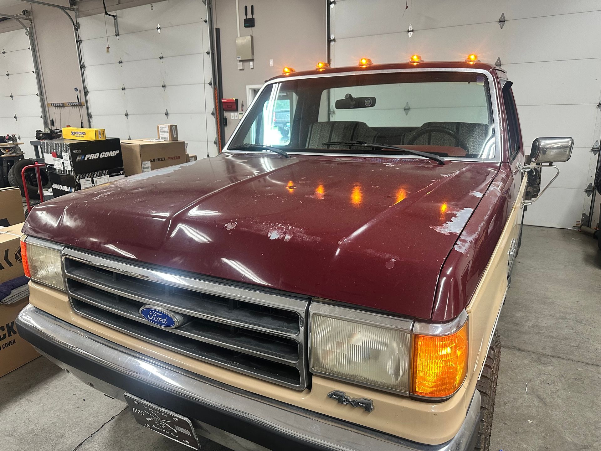 Maroon and tan Ford pickup truck with amber lights in a garage.