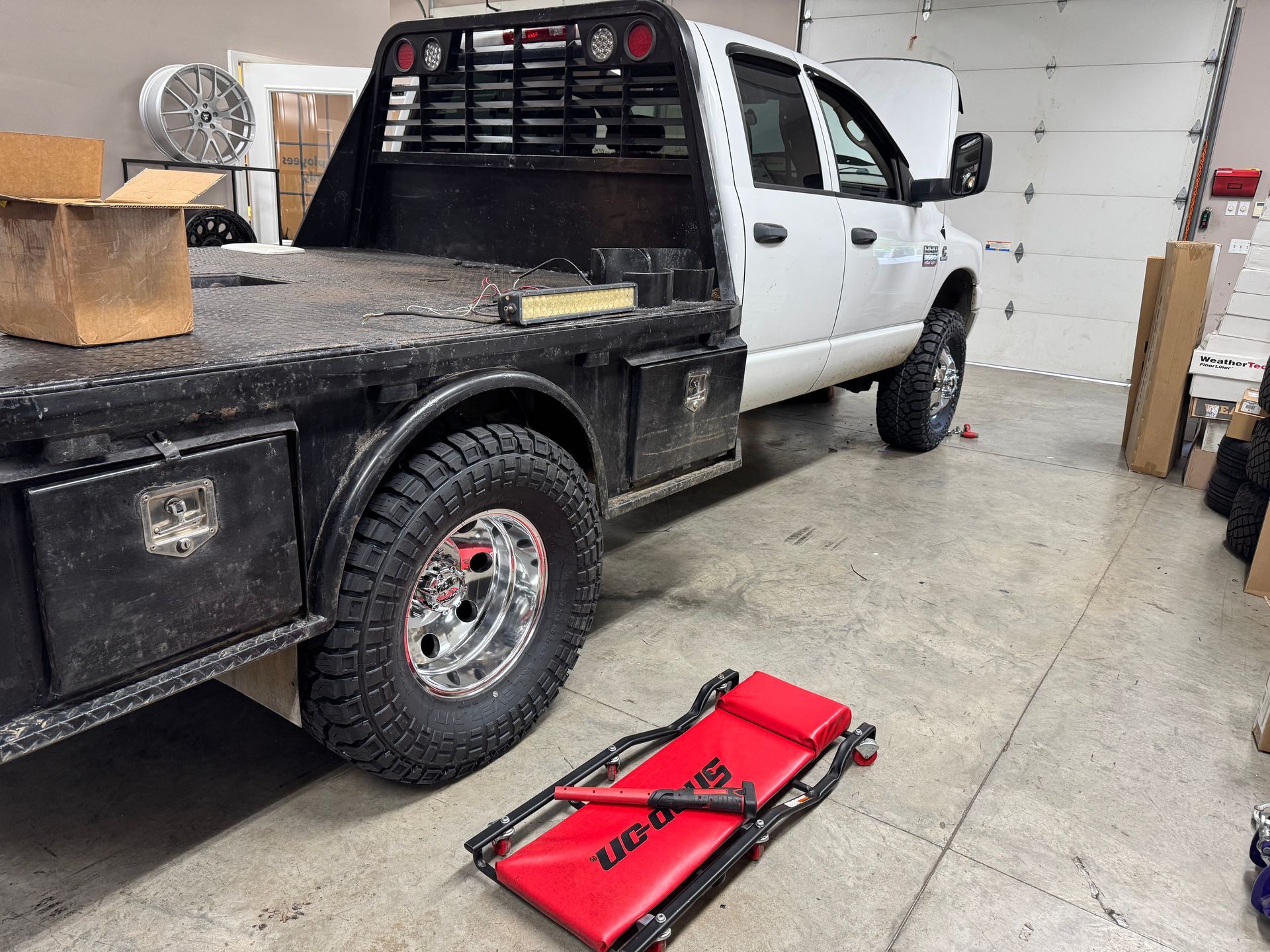 White flatbed truck in a garage with a red creeper.