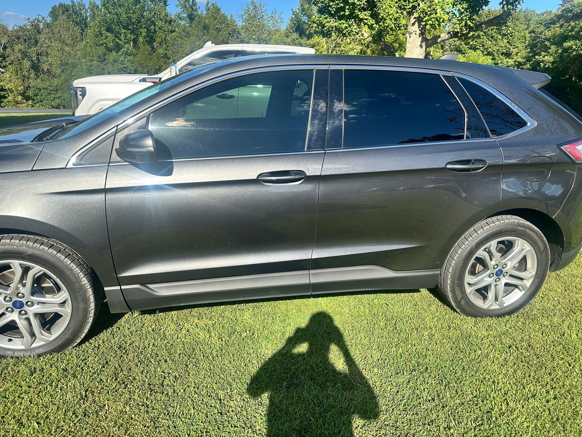 Dark gray Ford Edge parked on a grassy lawn; shadow of person taking photo visible.