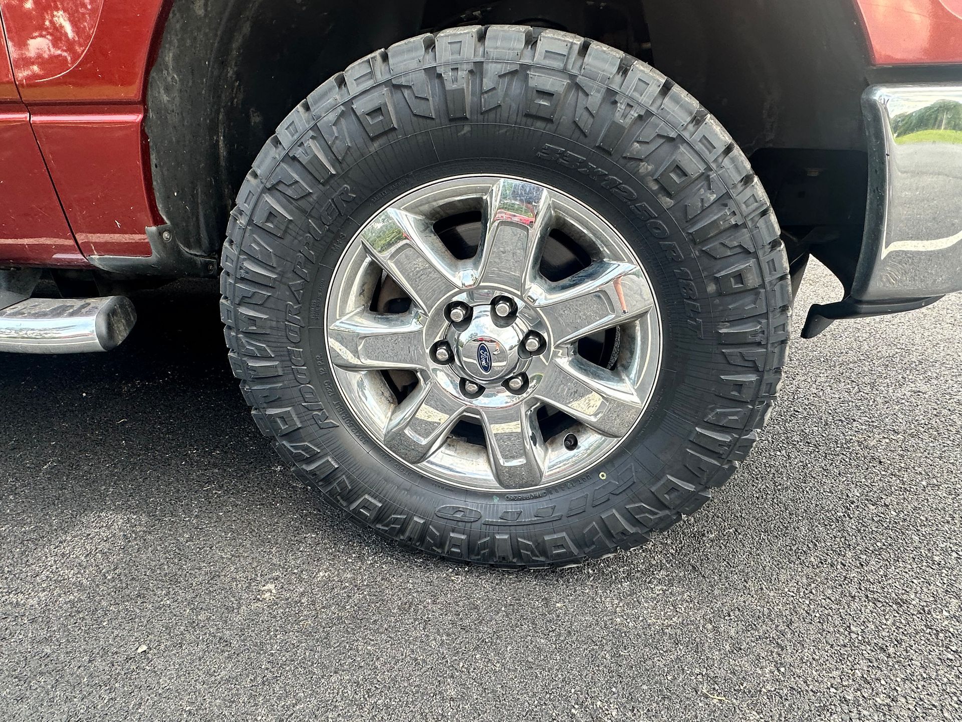 A red truck's tire and chrome rim on a paved road.