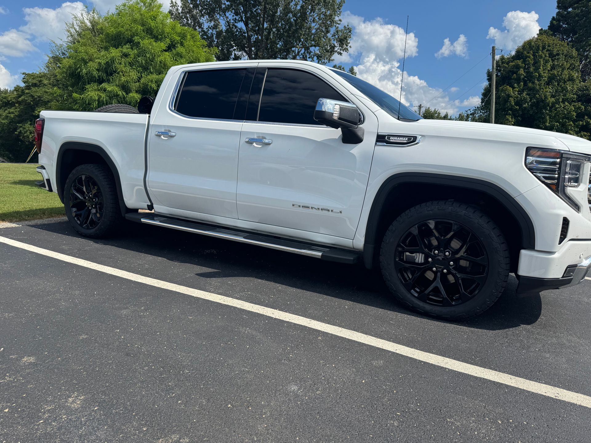 White GMC Sierra Denali pickup truck with black wheels parked in a lot.