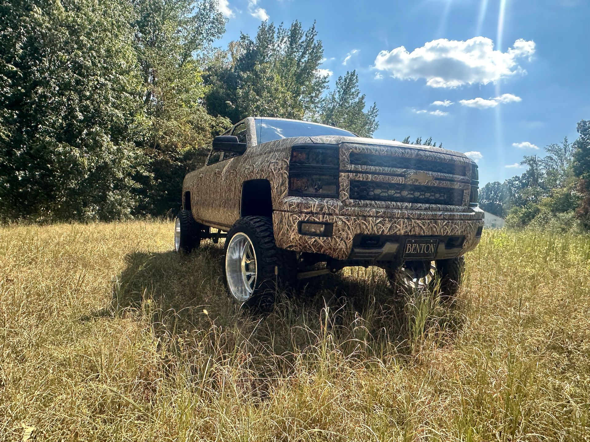 Camouflage pickup truck in a grassy field on a sunny day.