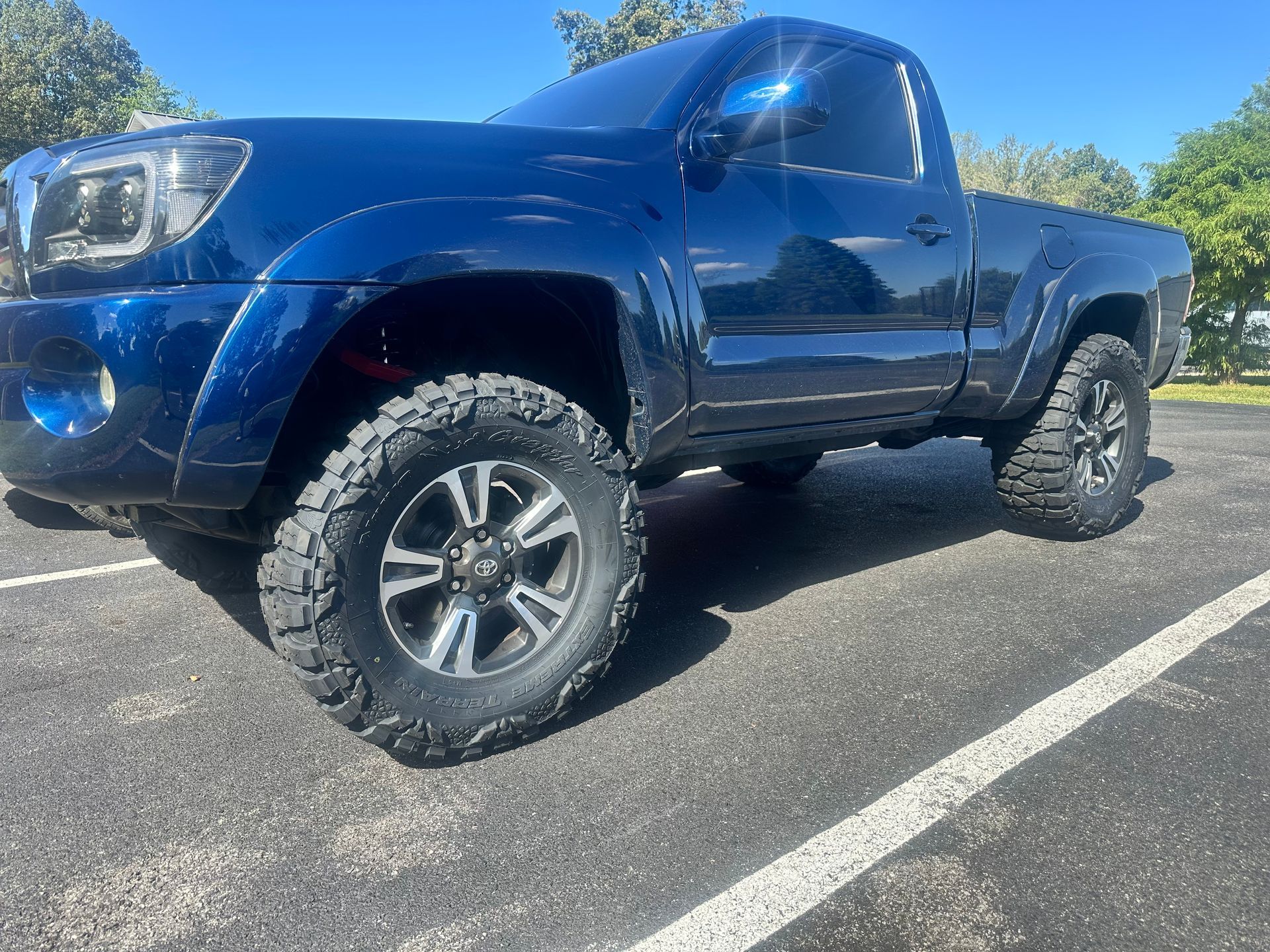 Blue Toyota Tacoma truck with large tires parked on pavement.