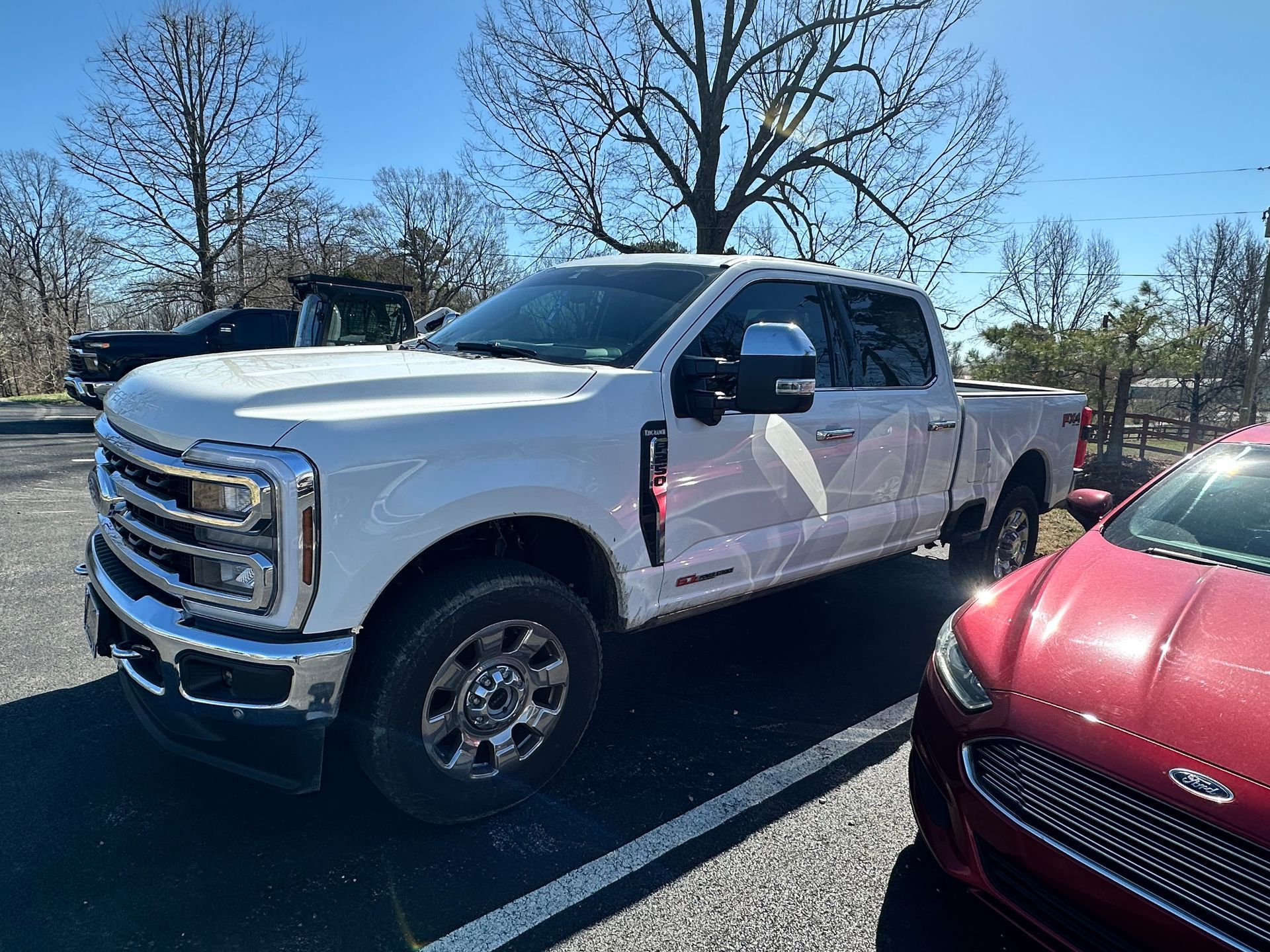 White Ford pickup truck parked next to a red car on an asphalt lot.