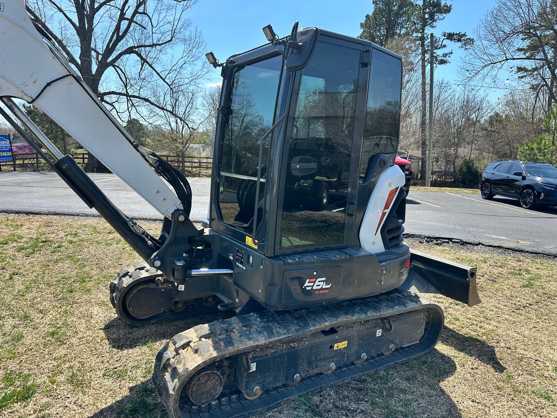 Bobcat excavator on grass with tracks, black cab, and white arm.