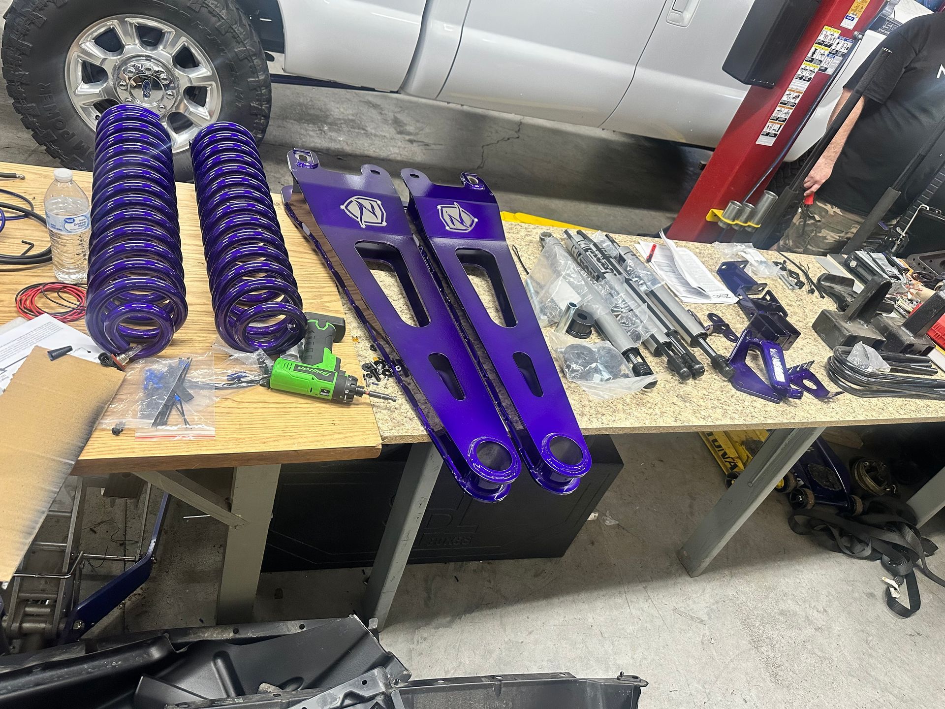 Purple truck suspension parts on a table, including springs and control arms. Garage setting.